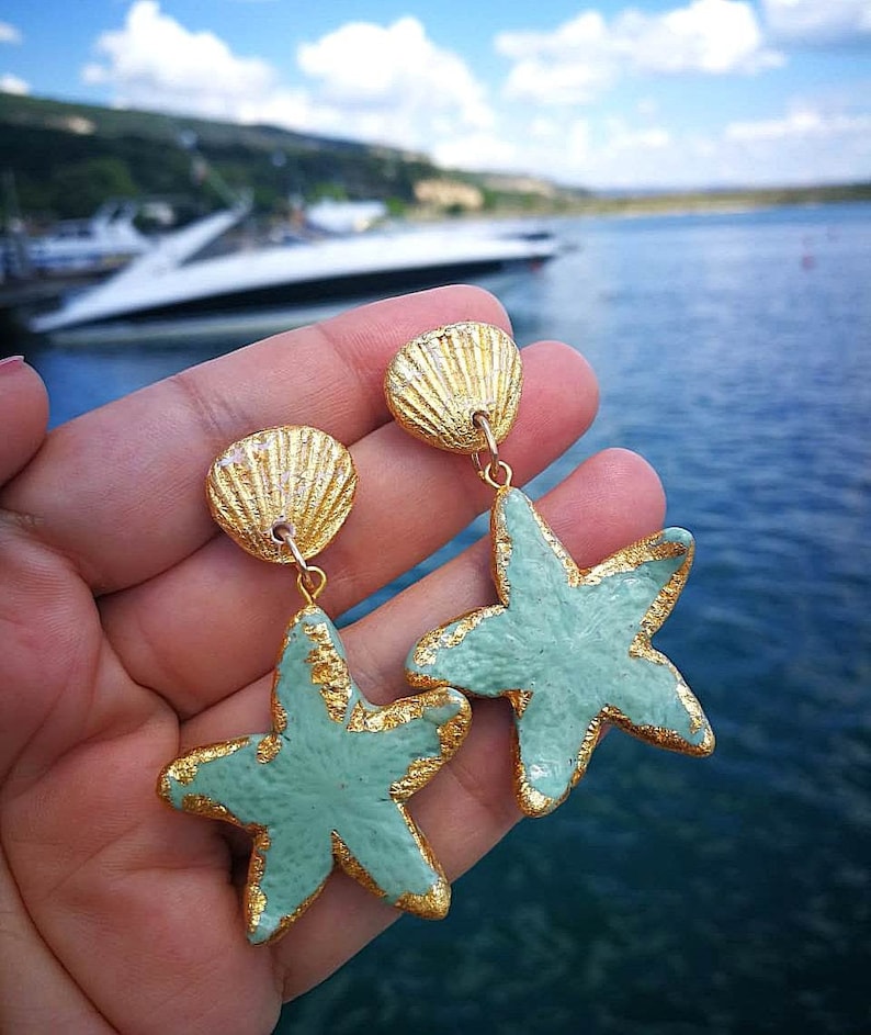 K&ouml;nnte beinhalten: Ein Paar goldene und hellblaue Ohrringe mit einem Muschel- und einem Seestern-Anh&auml;nger.