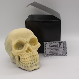 May include: A white chocolate skull in a black box with a label that reads "Sweet P Handmade Luxury Chocolate" and "Milk & White Chocolate Skull with a white and milk chocolate skull."