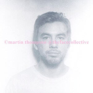 May include: A black and white photo of a person wearing a white t-shirt with the word "NIRVANA" printed on it. The photo is slightly blurry and has a grainy texture.