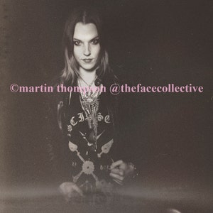 May include: A woman with long, dark hair is wearing a black leather jacket and a black t-shirt with a graphic design. The t-shirt has the word "Eclipse" written on it. The woman is looking at the camera. The image is in black and white and has a grainy texture. The text "@thefacecollective" is written in pink at the bottom of the image.