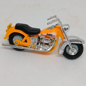 May include: A toy motorcycle in orange and silver, featuring a black seat and tires. The motorcycle has the Harley-Davidson logo and the number 1200 printed on the side. The handlebars and front fender are silver.