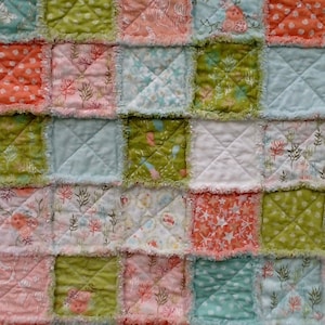 May include: A patchwork quilt with a variety of colors and patterns, including pink, blue, green, and white. The quilt is made of squares of fabric sewn together, and the edges are frayed.
