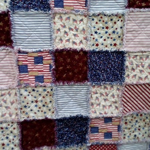 May include: A patchwork quilt made of various fabrics featuring red, white, and blue colors. The quilt is made of squares with different patterns, including stars, stripes, and flags.