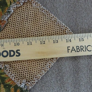 K&ouml;nnte beinhalten: Ein Lineal aus Holz, das in Zoll von 8 bis 17 markiert ist und die Worte "GOODS" und "FABRICS &" aufgedruckt hat. Das Lineal liegt auf einem braunen Stoff mit einem Rautenmuster.