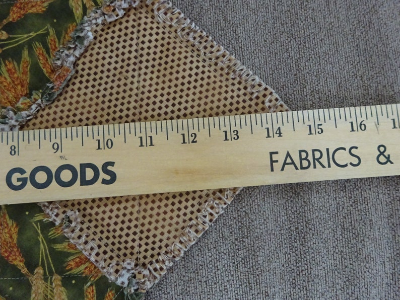 K&ouml;nnte beinhalten: Ein Lineal aus Holz, das in Zoll von 8 bis 17 markiert ist und die Worte "GOODS" und "FABRICS &" aufgedruckt hat. Das Lineal liegt auf einem braunen Stoff mit einem Rautenmuster.