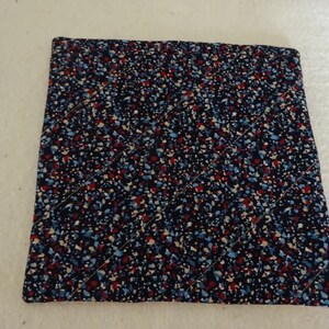 May include: A square, quilted hot pad with a black background and a pattern of small, colorful dots in red, blue, and white.