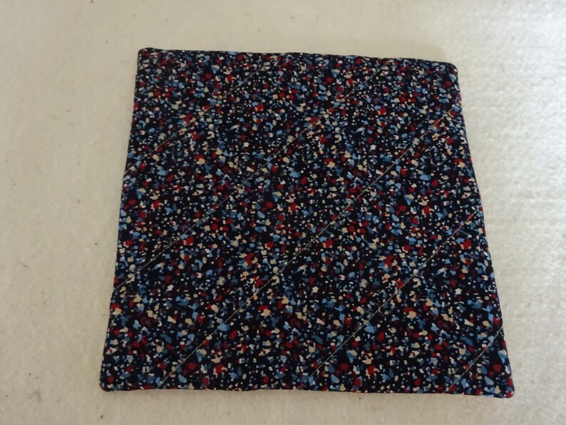 May include: A square, quilted hot pad with a black background and a pattern of small, colorful dots in red, blue, and white.
