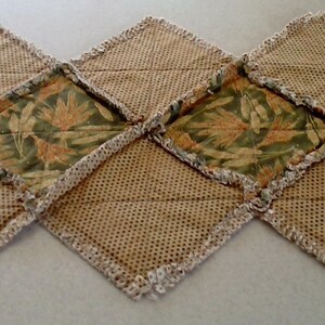 K&ouml;nnte beinhalten: Ein Tischl&auml;ufer aus braunem Sackleinen mit einem Blumenmuster. Der L&auml;ufer besteht aus Stoffquadraten, die mit einem wei&szlig;en H&auml;kelrand zusammengen&auml;ht sind.