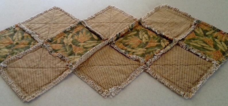 K&ouml;nnte beinhalten: Ein Tischl&auml;ufer aus braunem Sackleinen mit einem Blumenmuster. Der L&auml;ufer besteht aus Stoffquadraten, die mit einem wei&szlig;en H&auml;kelrand zusammengen&auml;ht sind.