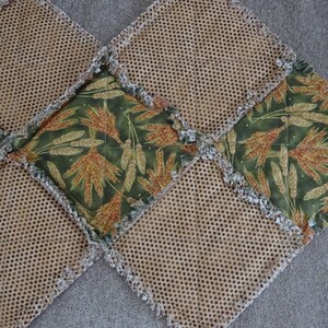 K&ouml;nnte beinhalten: Eine braune und gr&uuml;ne Patchwork-Decke mit ausgefransten Kanten. Die Decke besteht aus Quadraten aus verschiedenen Stoffen, darunter ein braunes Netzgewebe und ein gr&uuml;ner Stoff mit einem Weizenmuster.