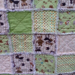 May include: A patchwork baby quilt with a woodland theme. The quilt is made of various fabrics with different patterns, including green, brown, and white. The quilt features a variety of woodland animals, including deer, bears, and squirrels.