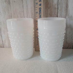 May include: Two white hobnail glasses with a textured surface. The glasses have a cylindrical shape and are next to a wooden ruler. The ruler has the text "EATING & SUPPLY" printed on it.