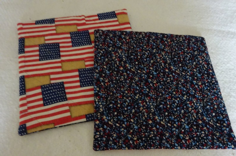 May include: Two quilted pot holders. One is red, white, and blue with a pattern of American flags. The other is navy blue with red, white, and blue speckles.
