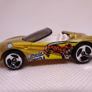 May include: A gold toy convertible car with black wheels and a black windshield. The car has a yellow and orange tiger graphic and the words "Davis Tigers" on the side. The interior is white.