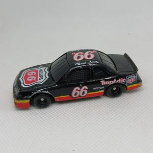 May include: A black toy race car with the number "66" in red and white on the sides and roof. The car has sponsor logos, including "Phillips 66" and "TropArtic Motor Oil". The car has a spoiler and red and yellow accents.