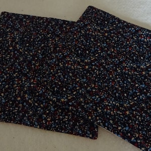 May include: Two blue, red, and white patterned fabric pot holders. The pot holders are quilted and have a square shape.