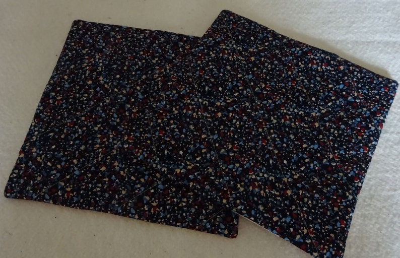 May include: Two blue, red, and white patterned fabric pot holders. The pot holders are quilted and have a square shape.