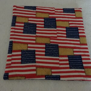 May include: A red, white, and blue quilted pot holder with a pattern of American flags and tan squares.