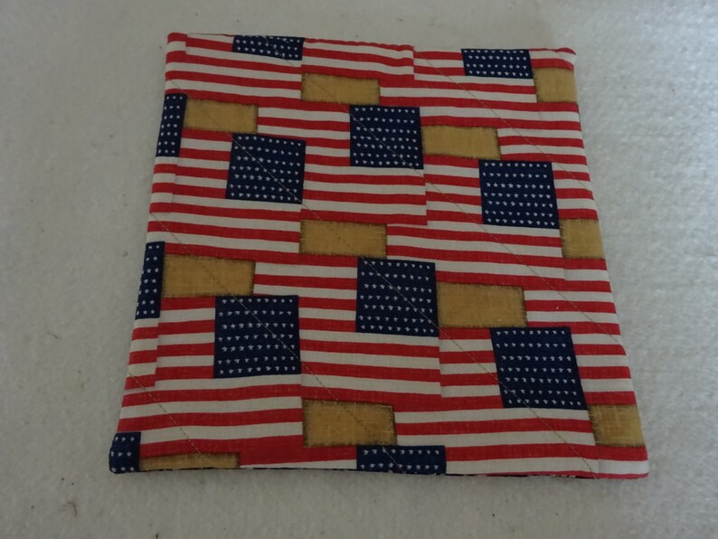 May include: A red, white, and blue quilted pot holder with a pattern of American flags and tan squares.