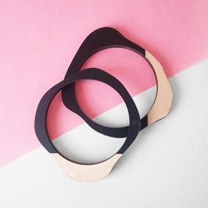 May include: Two black wooden bangles with a natural wood finish on the inside edge. The bangles are stacked on top of each other.
