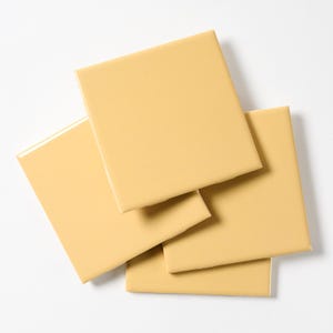 May include: Four square ceramic tiles in a pale yellow color. The tiles are stacked on top of each other.