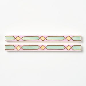 May include: Two decorative, rectangular tiles with a repeating geometric pattern. The tiles have a light pink background with light green and yellow shapes outlined in brown. The tiles are displayed on a white background.