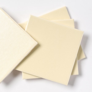 May include: A collection of square, off-white tiles with a slightly textured surface. The tiles are stacked and arranged, showcasing their shape and color against a white background. The tiles appear to be made of a durable material.