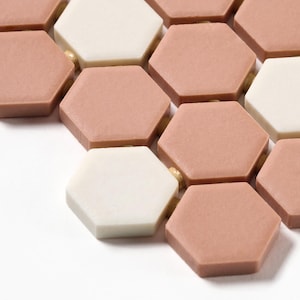 May include: Close-up of a pattern of pink and white hexagonal tiles. The tiles are arranged in a staggered pattern, with the pink tiles in the center and the white tiles on the edges.