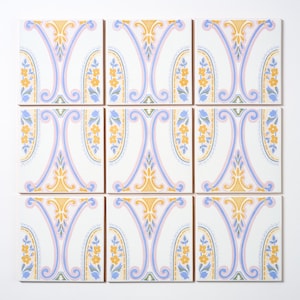 May include: Nine square ceramic tiles arranged in a grid. Each tile features a symmetrical design with a central blue and pink motif, accented by yellow floral elements and a white background. The tiles are likely for home decor.