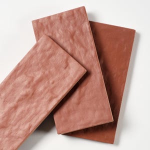 May include: Three rectangular terracotta-colored tiles arranged on a white surface. The tiles have a textured, slightly uneven surface, and vary slightly in shade. The tiles are likely for use in construction or interior design.