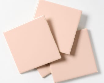 May include: Four pale pink square ceramic tiles stacked on top of each other.