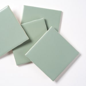 May include: Four square ceramic tiles in a pale sage green color. The tiles are arranged in a staggered pattern.