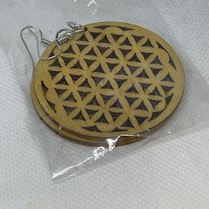 May include: A pair of wooden earrings with a flower of life design. The earrings are brown and have a silver hook.