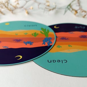 Pu&ograve; includere: Due sottobicchieri rotondi, colorati e illustrati con una scena del deserto. Un sottobicchiere dice "pulito" e l'altro dice "sporco".
