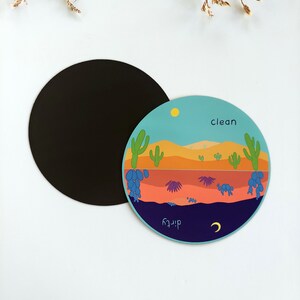 Pu&ograve; includere: Un magnete rotondo blu, arancione e verde con una scena del deserto. Il magnete ha le parole "pulito" e "sporco" scritte su di esso.