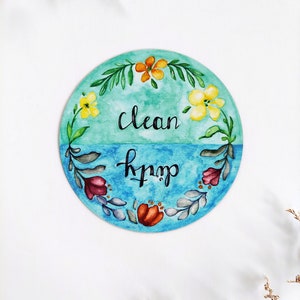 Pu&ograve; includere: Un cartello rotondo dipinto ad acquerello con sfondo blu e verde. Il cartello &egrave; decorato con fiori e foglie. Il testo sul cartello recita "clean" e "dirty".