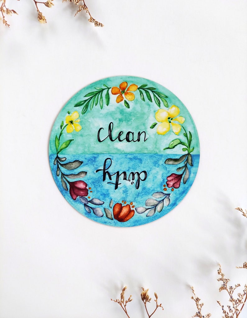 Pu&ograve; includere: Un cartello rotondo dipinto ad acquerello con sfondo blu e verde. Il cartello &egrave; decorato con fiori e foglie. Il testo sul cartello recita "clean" e "dirty".