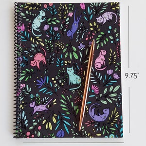 Op de afbeelding: Een zwart spiraalnotitieblok met een kleurrijk bloemen- en kattenpatroon. Het notitieblok meet 19,05 cm bij 24,76 cm.