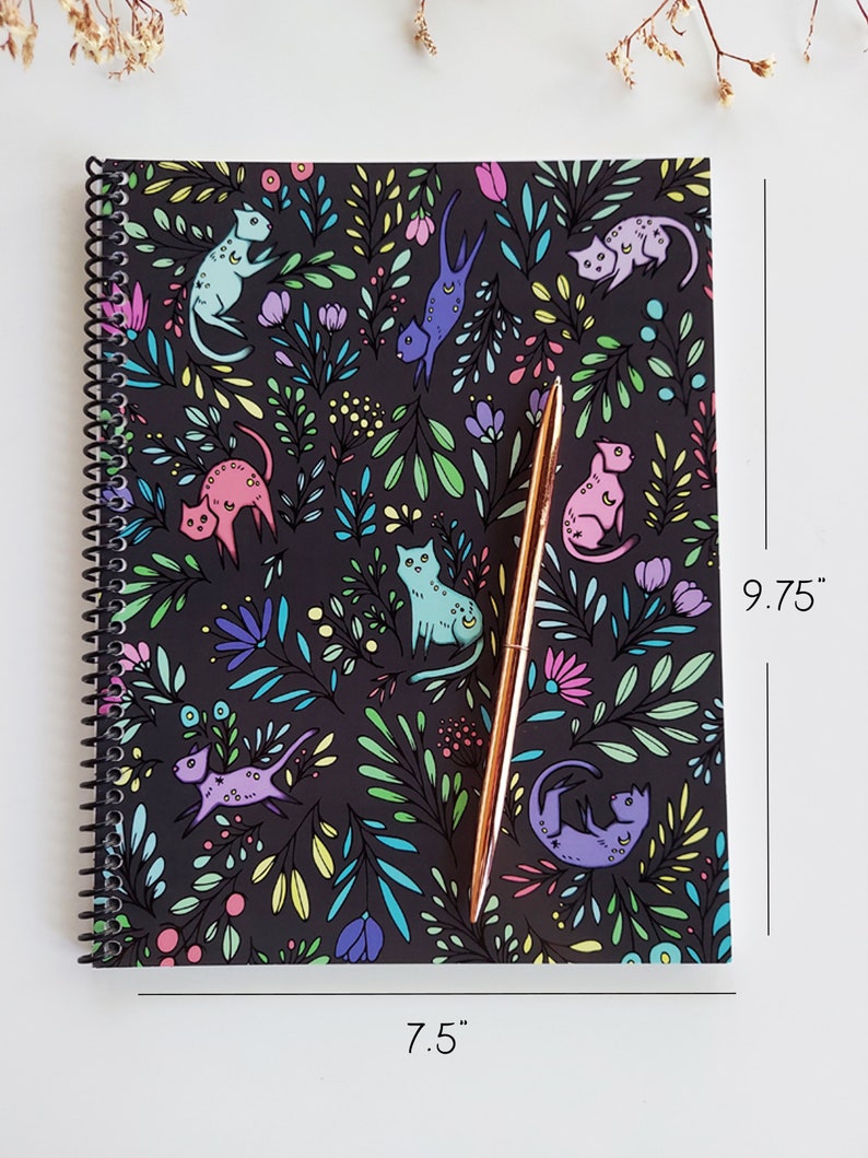 Op de afbeelding: Een zwart spiraalnotitieblok met een kleurrijk bloemen- en kattenpatroon. Het notitieblok meet 19,05 cm bij 24,76 cm.