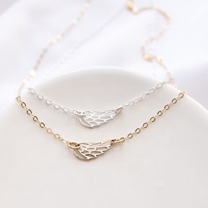 May include: Two delicate necklaces featuring small, open-work wing charms. One necklace is crafted from silver-toned metal, while the other is gold-toned. Both chains are thin and link-style, showcasing a minimalist design with a polished finish.