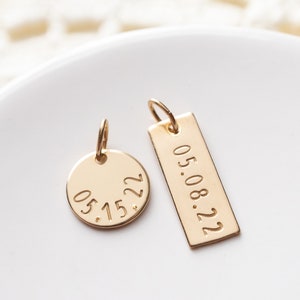 A small disc and a rectangle are hand stamped with custom dates. They are placed next to each other on a ring dish.