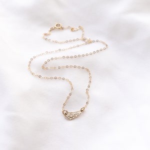 May include: A delicate gold-toned necklace featuring a small, open-work wing pendant. The chain is composed of thin, circular links and includes a small round spring-ring clasp at the back, creating a simple and refined piece of jewelry.