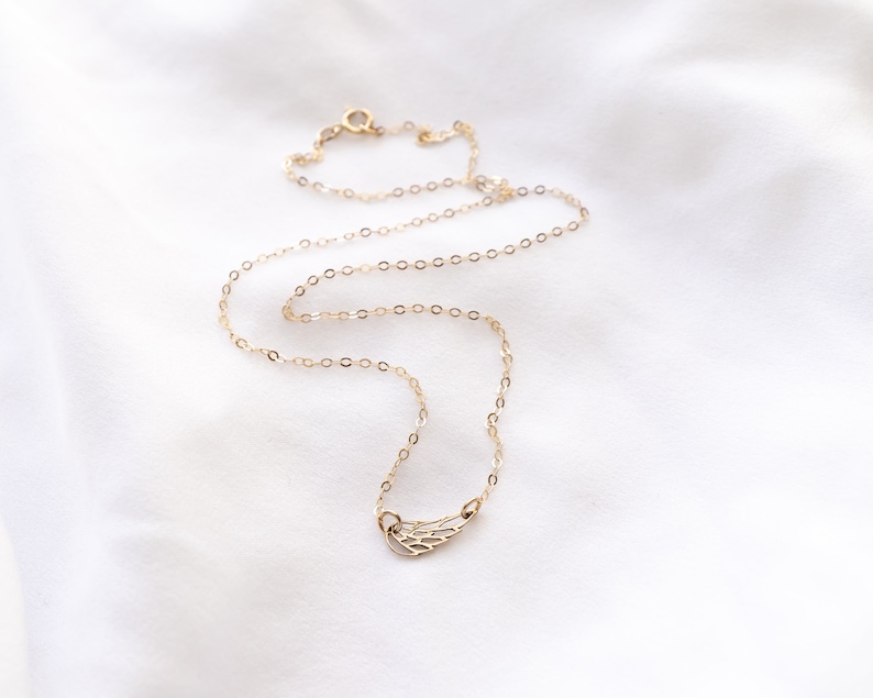 May include: A delicate gold-toned necklace featuring a small, open-work wing pendant. The chain is composed of thin, circular links and includes a small round spring-ring clasp at the back, creating a simple and refined piece of jewelry.