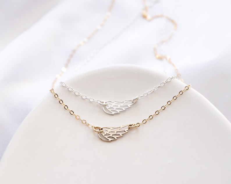 May include: Two delicate necklaces featuring small, open-work wing charms. One necklace is crafted from silver-toned metal, while the other is gold-toned. Both chains are thin and link-style, showcasing a minimalist design with a polished finish.