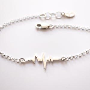 May include: A silver chain bracelet with a heart beat design charm. The bracelet is made of a delicate chain and has a lobster clasp closure.