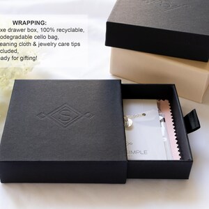 May include: A black square drawer box with a debossed letter S logo on the lid, partially open to reveal a white jewelry card and a pink cleaning cloth inside. A second beige drawer box is stacked behind it, both featuring black pull tabs.