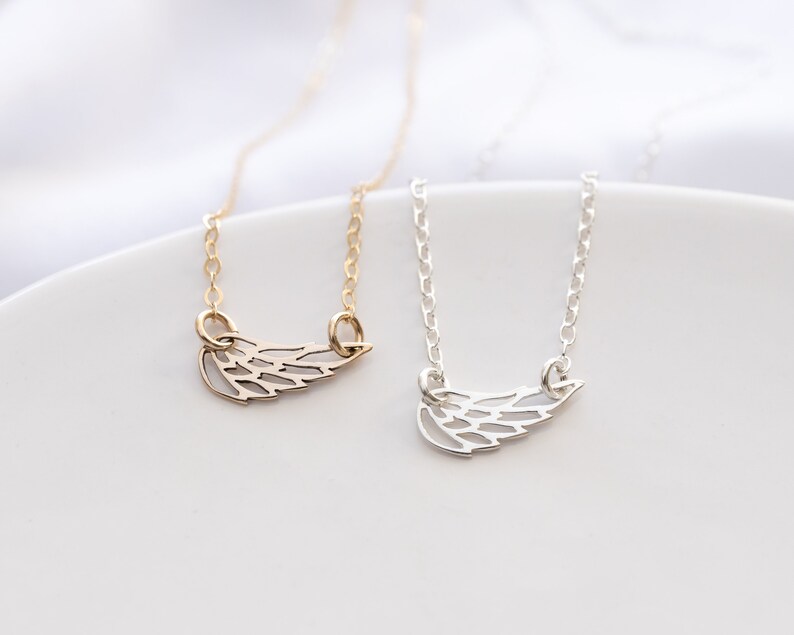 May include: Two necklaces featuring delicate wing-shaped pendants. One necklace is gold-toned with a matching gold chain, and the other is silver-toned with a matching silver chain. Both pendants have a cut-out design resembling bird feathers.