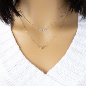 May include: A layered necklace set featuring two delicate chains. The top chain is silver-toned with a small wing-shaped pendant, while the bottom chain is gold-toned and also features a small wing-shaped pendant. Both chains have a fine link design.