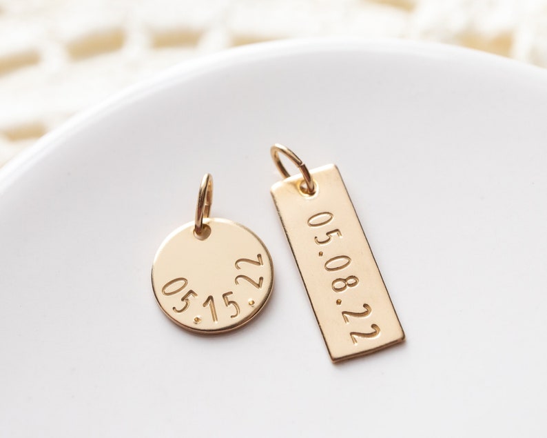 A small disc and a rectangle are hand stamped with custom dates. They are placed next to each other on a ring dish.