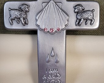 May include: Silver cross with a shell, two lambs, and the words "Baptized in Christ" and "I am a child of God".
